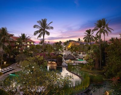 Tropical resort with multiple pools, palm trees, and lush greenery at dusk under a colorful sky.
