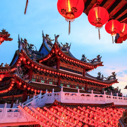 Traditional Chinese temple adorned with numerous red lanterns glowing at dusk, vibrant and ornate architectural details.