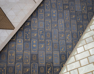 Abstract geometric design with a blue and gold Egyptian hieroglyphics pattern. Triangular shapes and light stone tiles add contrast and depth.
