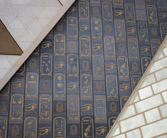 Abstract geometric design with a blue and gold Egyptian hieroglyphics pattern. Triangular shapes and light stone tiles add contrast and depth.