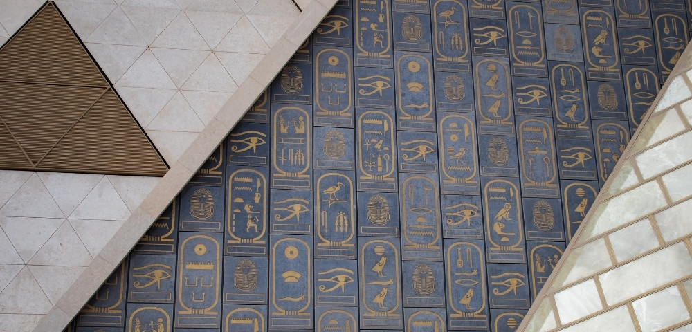 Abstract geometric design with a blue and gold Egyptian hieroglyphics pattern. Triangular shapes and light stone tiles add contrast and depth.