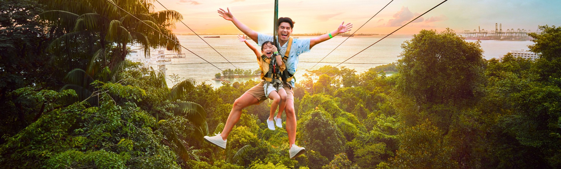Father and child joyfully ziplining over lush green trees with arms wide open. A serene sunset over a distant water body adds warmth and excitement.