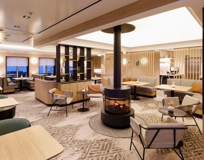 A modern lounge area with comfortable seating, tables, and a central fireplace.