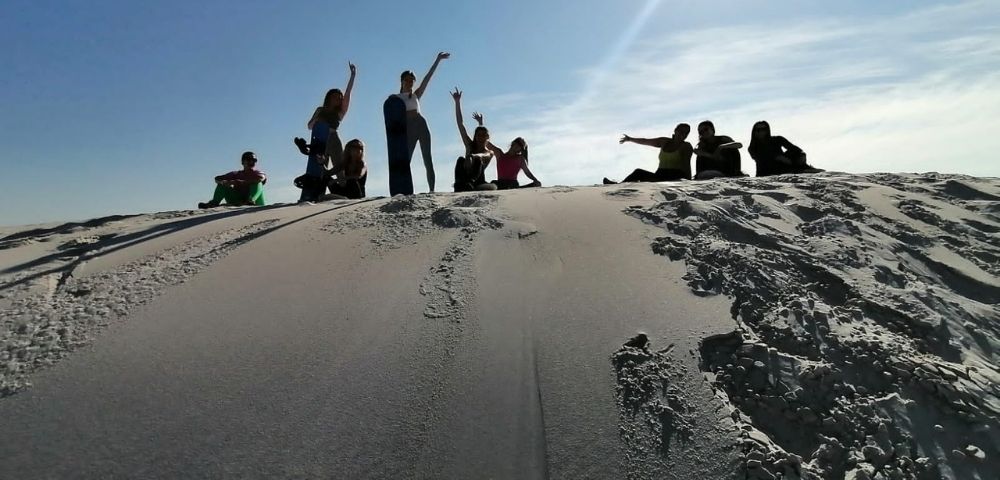 A group of people are posing and sitting on a sandy dune under a clear blue sky.