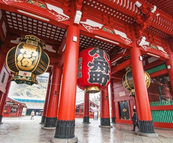 Large, ornate, traditional Japanese lanterns hang from the brightly painted red pillars of a temple entrance.