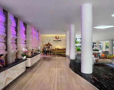 The lobby of a modern hotel with a unique textured wall illuminated by purple light, a grand piano, and prominent white columns.