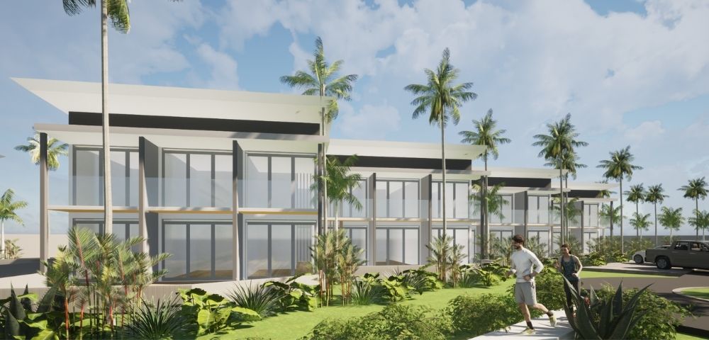 A modern, multi-story building with large windows and balconies is surrounded by lush tropical foliage and palm trees, with two people jogging on a path in the foreground under a cloudy blue sky.