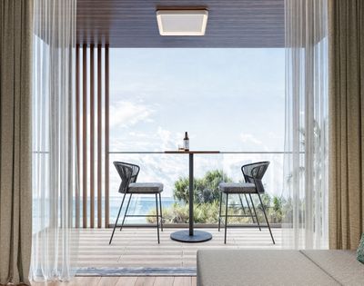 A contemporary balcony with two black wicker bar stools and a small circular table with a bottle and glass, overlooking the ocean.
