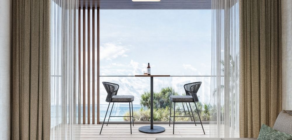 A contemporary balcony with two black wicker bar stools and a small circular table with a bottle and glass, overlooking the ocean.