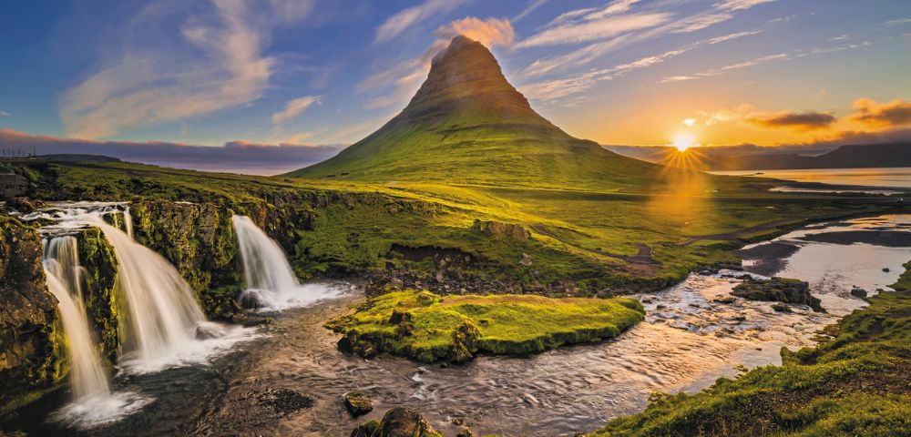 A picturesque panorama of Kirkjufell mountain in Iceland at sunset, with cascading waterfalls in the foreground.