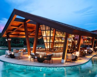 Contemporary poolside bar with sleek wooden architecture and warm lighting, surrounded by water. Cozy seating and a serene evening ambiance.
