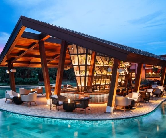 Contemporary poolside bar with sleek wooden architecture and warm lighting, surrounded by water. Cozy seating and a serene evening ambiance.