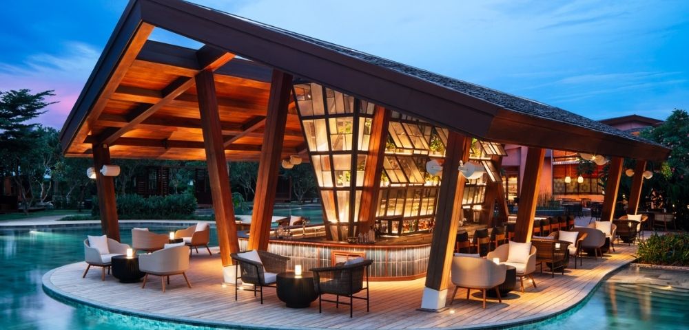 Contemporary poolside bar with sleek wooden architecture and warm lighting, surrounded by water. Cozy seating and a serene evening ambiance.