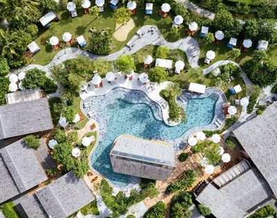 Top-down view of a beach club with multiple pools, greenery, and surrounding structures