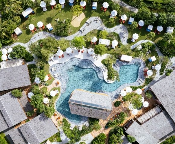 Top-down view of a beach club with multiple pools, greenery, and surrounding structures