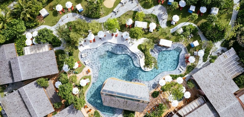 Top-down view of a beach club with multiple pools, greenery, and surrounding structures