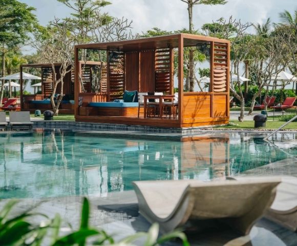 Wooden pavilion structure over a pool area with seating and shaded relaxation space