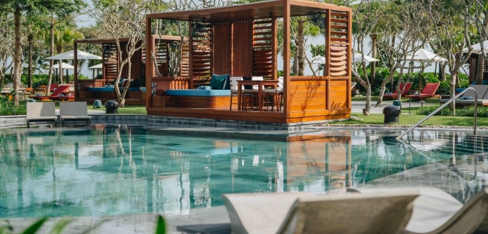 Wooden pavilion structure over a pool area with seating and shaded relaxation space