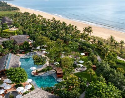 Aerial view of a beachfront resort with palm trees, pools, and shoreline in Hoi An