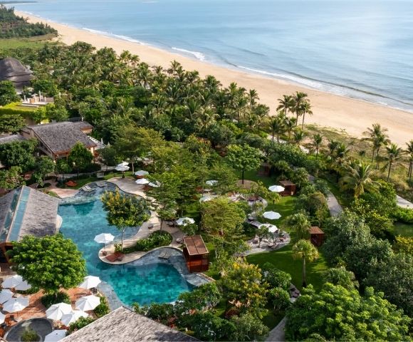 Aerial view of a beachfront resort with palm trees, pools, and shoreline in Hoi An