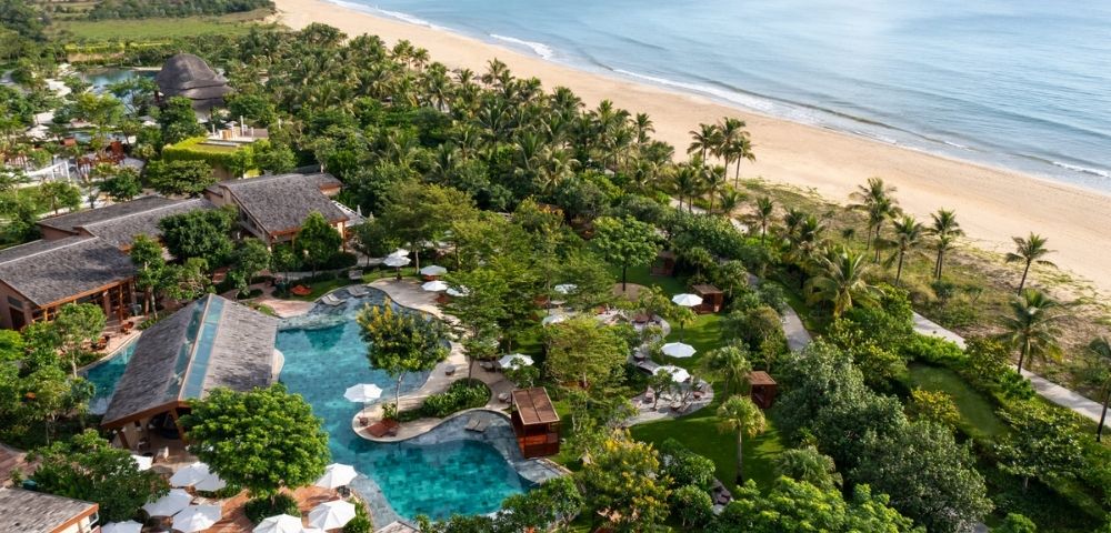 Aerial view of a beachfront resort with palm trees, pools, and shoreline in Hoi An