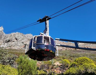 A cable car ascends a mountain against a clear blue sky.