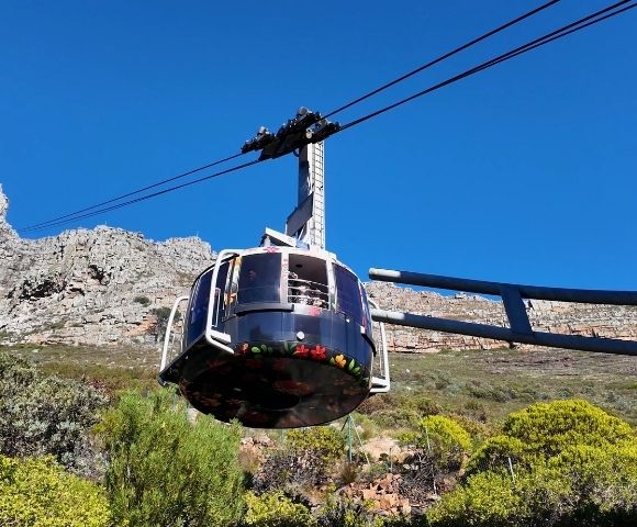 A cable car ascends a mountain against a clear blue sky.