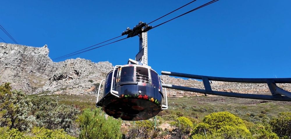 A cable car ascends a mountain against a clear blue sky.
