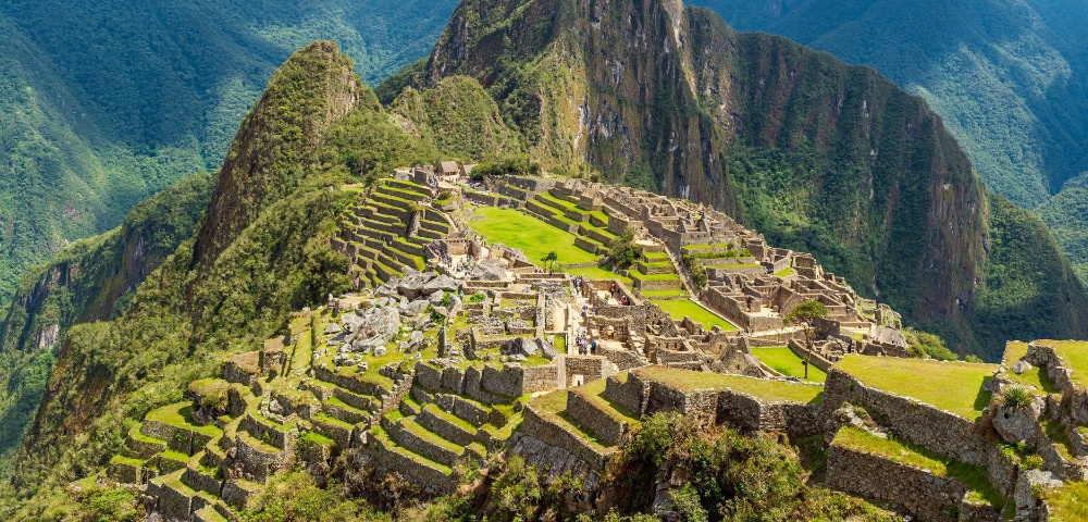 Aerial view of Machu Picchu, showcasing ancient stone terraces and ruins set on a lush, green mountain backdrop. The scene conveys a sense of awe and history.