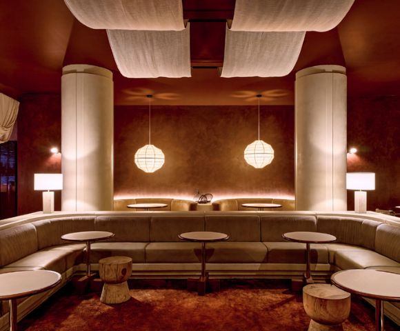 A modern lounge area with a curved sofa, round tables, and minimalist pendant lights.