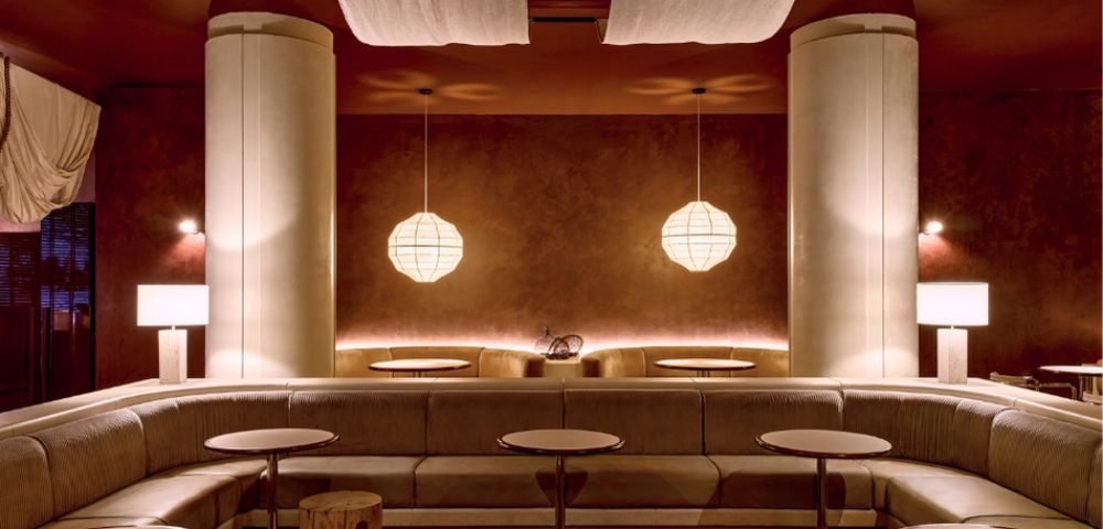 A modern lounge area with a curved sofa, round tables, and minimalist pendant lights.