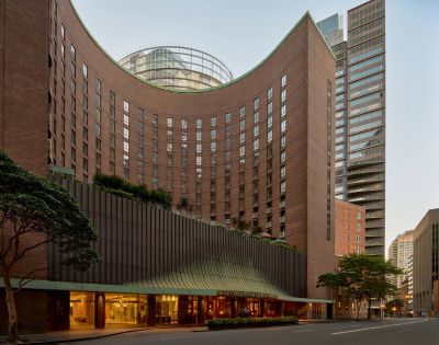 Curving brick hotel building with a modern facade and entrance, set against a city skyline.