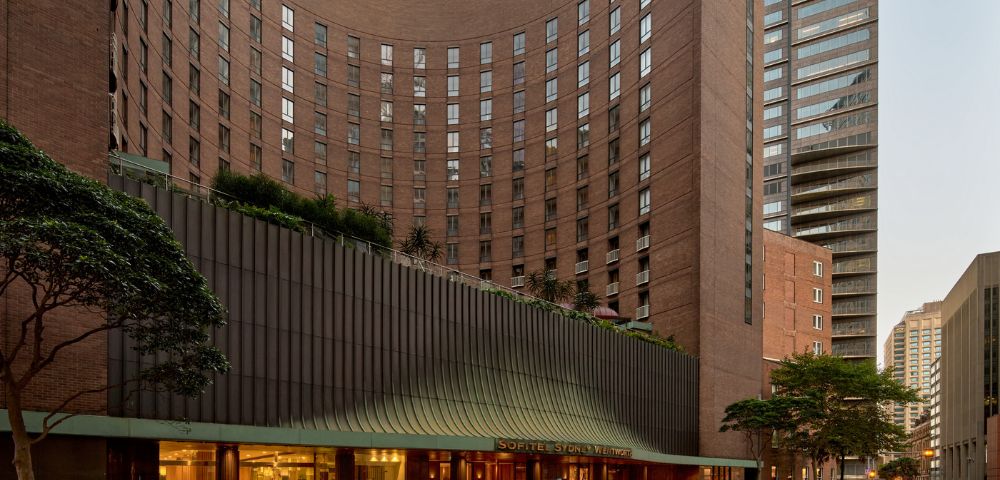 Curving brick hotel building with a modern facade and entrance, set against a city skyline.
