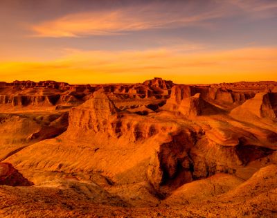 A wide, arid landscape of eroded rock formations bathed in the warm, orange glow of sunset.