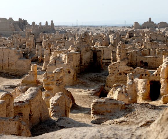 Ruined ancient mud-brick structures in a desert landscape, with crumbling walls and doorways.