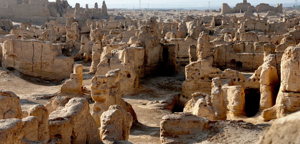 Ruined ancient mud-brick structures in a desert landscape, with crumbling walls and doorways.