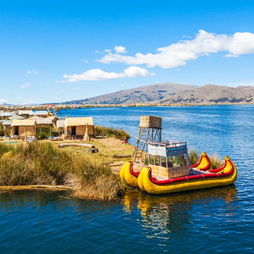 Floating reed island on Lake Titicaca with traditional huts, vibrant yellow reed boat, and distant mountains under a bright blue sky. Peaceful ambiance.