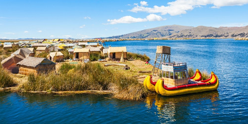 Floating reed island on Lake Titicaca with traditional huts, vibrant yellow reed boat, and distant mountains under a bright blue sky. Peaceful ambiance.