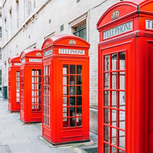 Row of classic red British telephone booths against a light brick wall, conveying nostalgia and iconic British culture.