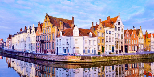 Picturesque canal lined with colorful, ornate Flemish gabled buildings in Bruges. The serene water reflects these charming architectural facades.