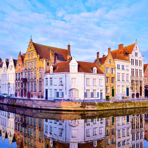 Picturesque canal lined with colorful, ornate Flemish gabled buildings in Bruges. The serene water reflects these charming architectural facades.