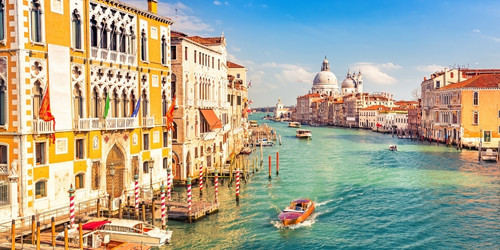 Majestic Venice canal scene with colorful historic buildings, gondolas, and boats on vibrant turquoise water under a clear blue sky with distant domes.
