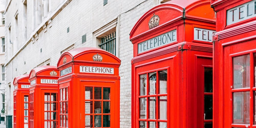 Row of classic red British telephone booths against a light brick wall, conveying nostalgia and iconic British culture.