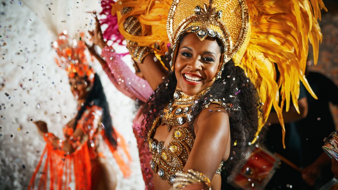 Dancers wearing vibrant, ornate costumes with large feathered headdresses perform energetically amid falling confetti at a festive celebration.