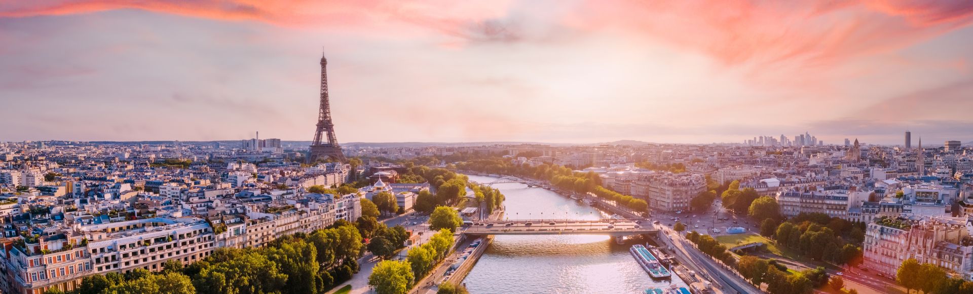 A panoramic view of Paris at sunset, featuring the Eiffel Tower on the left, the Seine River flowing through the city, and a vibrant, colorful sky.