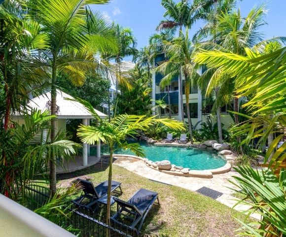 Tropical resort courtyard with a freeform swimming pool, lounge chairs, and lush palm trees.