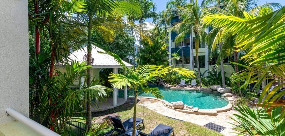 Tropical resort courtyard with a freeform swimming pool, lounge chairs, and lush palm trees.