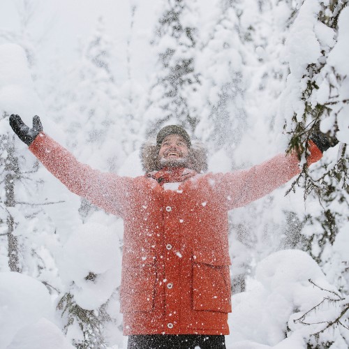 A person joyfully throws snow into the air amidst snow-covered trees, conveying a sense of excitement and winter wonderland.