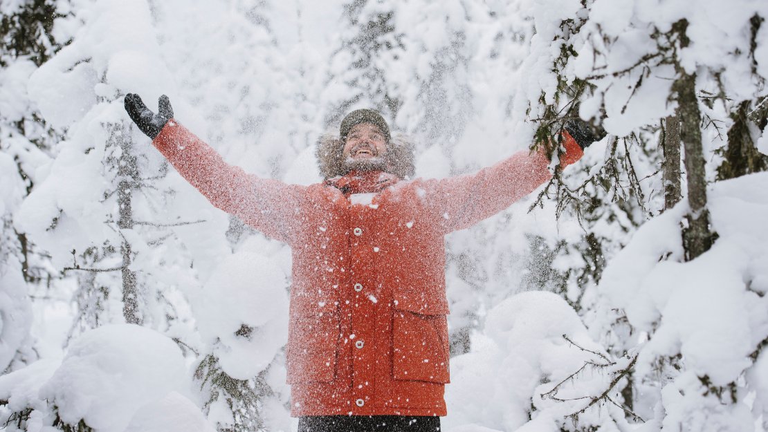 A person joyfully throws snow into the air amidst snow-covered trees, conveying a sense of excitement and winter wonderland.