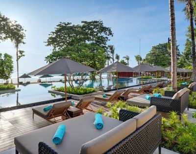 Resort poolside with lounge chairs, umbrellas, and a pool overlooking a beach.